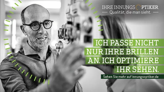 Ein Mann mit Bart, Brille und Glatze lächelt und blickt durch ein optisches Gerät. Seine Hände befinden sich in der Nähe des Geräts, was darauf hindeutet, dass er es aktiv benutzt oder vorführt. Die Umgebung scheint eine professionelle Optikerumgebung zu sein. Der Textüberlagerung lautet: „ICH PASSE NICHT NUR IHRE BRILLEN AN. ICH OPTIMIERE IHR SEHEN.“